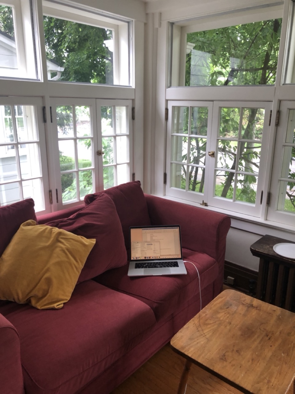 corner of a cozy porch, pink couch and bright windows, with a laptop open. 